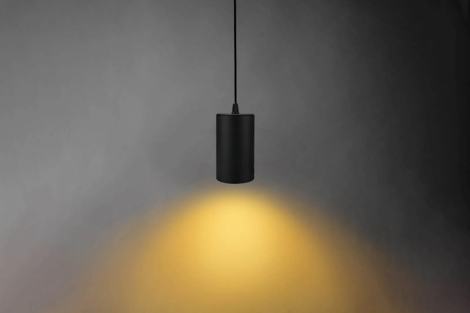 Cilindro suspendido negro Sedona Collection con una mancha de luz cálida en una pared oscura