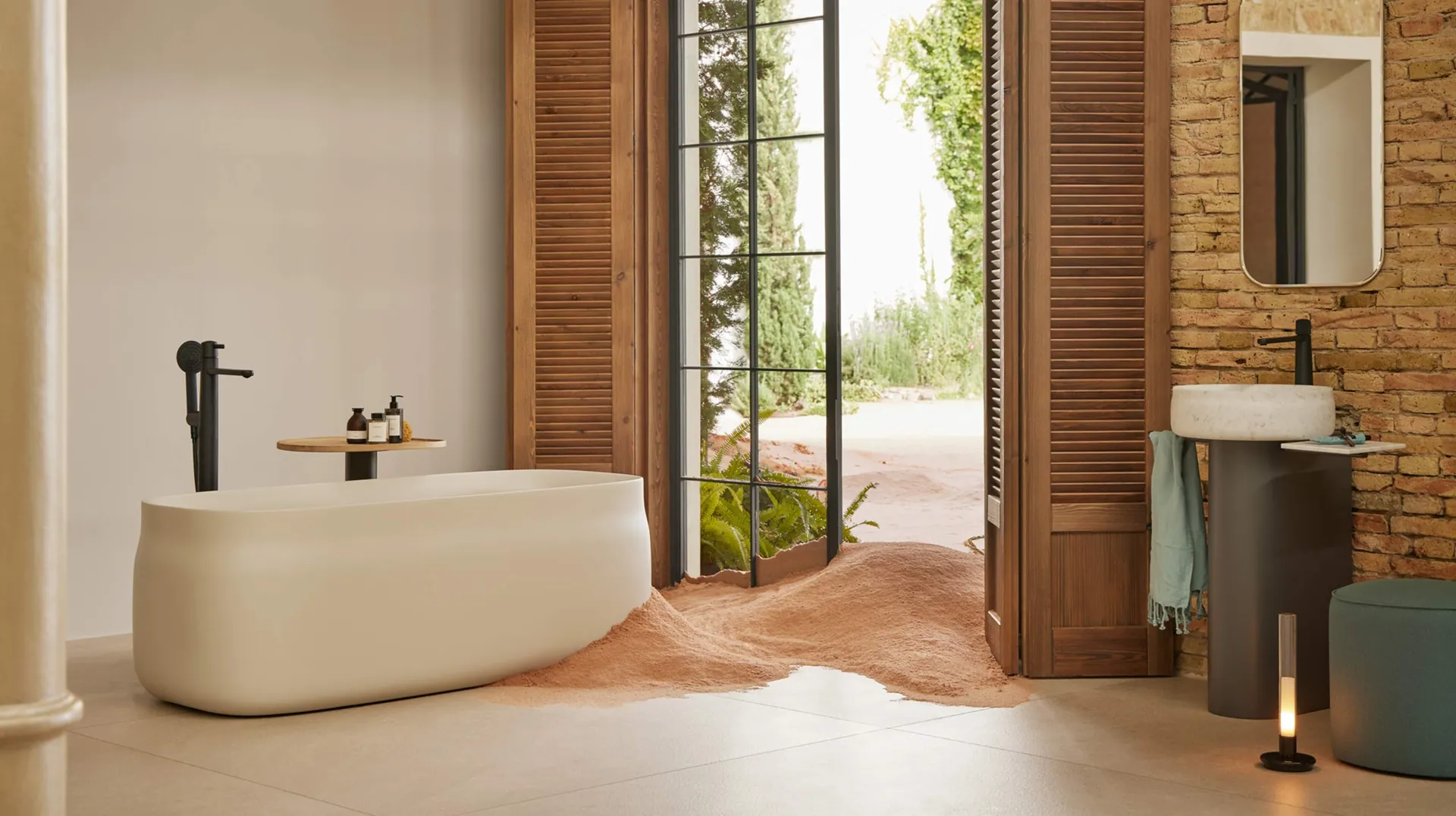 Bañera exenta Sanycces Duna y lavabo de columna junto a una pared de ladrillo